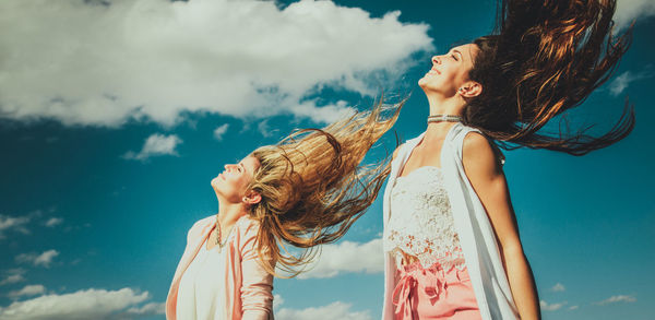 Cheerful young friends tossing hair against sky