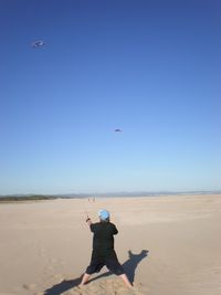 Rear view of man flying kite at beach against clear blue sky