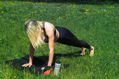 Young caucasian blond-haired woman in sportswear is doing yoga in public park. outdoor workout.