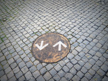 High angle view of arrow symbol over manhole lid on footpath