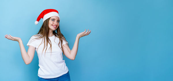 Young woman wearing hat standing against blue wall