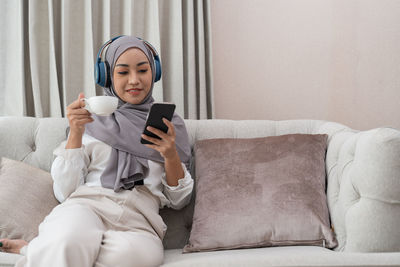 Young woman using mobile phone while lying on bed at home