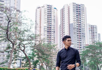 Thoughtful young man standing against trees in city