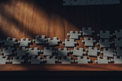 Sunlight from the window falls on white puzzle pieces on a wooden table, selective focus.