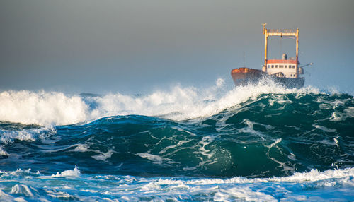 Abandoned ship in the stormy sea with big wind waves during sunset.