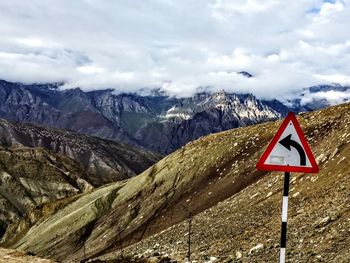 Road sign by mountains against sky