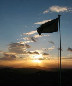 Low angle view of silhouette flag waving against mountains at sunset