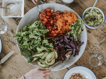 Cropped hands taking food from bowl at wooden table