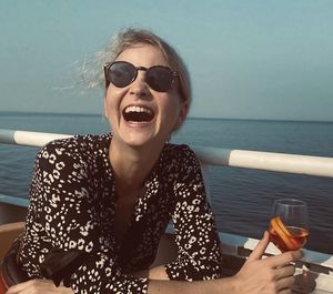 Portrait of young laughing woman wearing sunglasses against sea