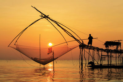 Silhouette fishing net on lake against sky during sunset