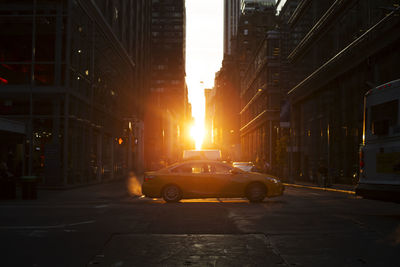 Vehicles on street amidst buildings during sunset