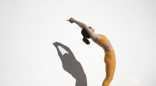 Female athlete doing backbend stretching exercise by a white wall in the sun