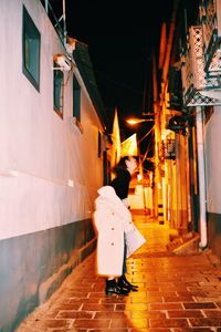 Rear view of woman walking on illuminated street at night