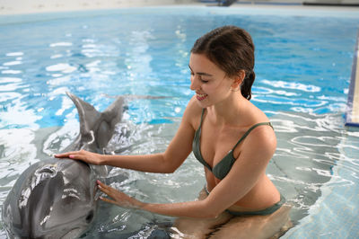 Smiling young woman with dolphin in swimming pool
