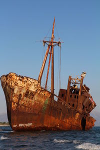 Damaged ship in sea against clear blue sky