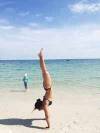 Woman in bikini practicing handstand on shore at beach