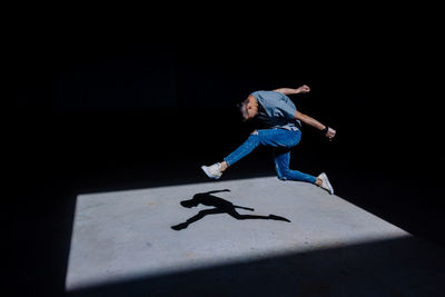 Sunlight falling on young man jumping in darkroom
