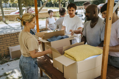 Male and female volunteers discussing while sorting blankets in cardboard boxes on table during charity drive at communi