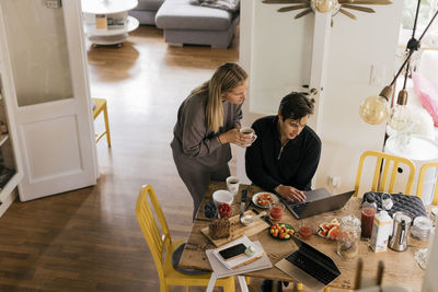 Male and female freelancers working on laptop while having breakfast at home