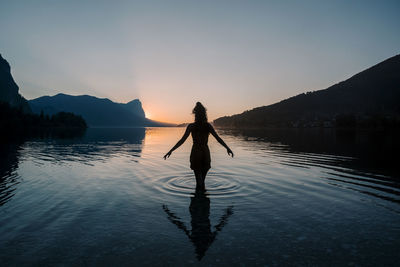 Silhouette man standing in lake against sky during sunset