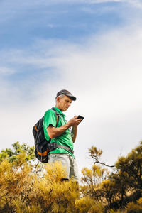 Senior backpacker using smart phone on cliff against sky