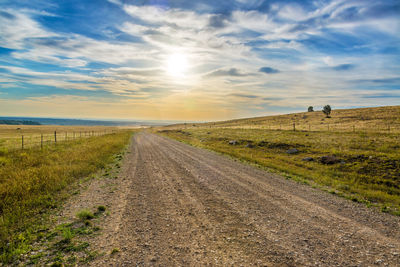 Road amidst field against sky during sunset