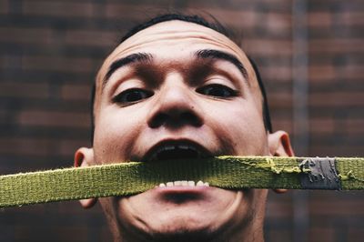 Portrait of man carrying belt in mouth against wall