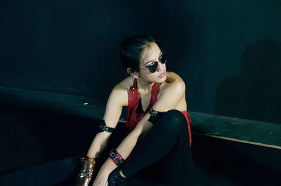 High angle view of young woman looking away while sitting against black wall