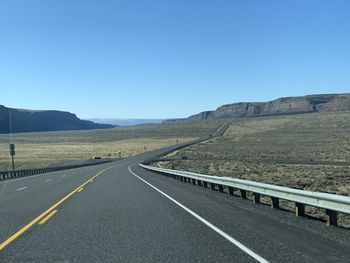 Road leading towards mountains against clear sky