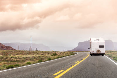 Vehicles on road against cloudy sky