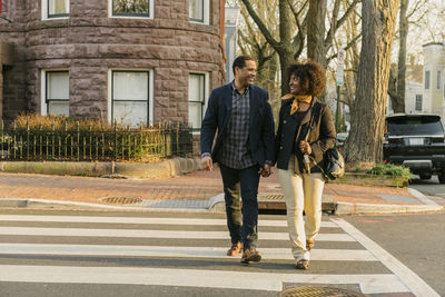 Full length of happy couple holding hands while crossing road