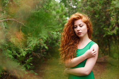 Portrait red beautiful young woman, against green summer park. in green dress