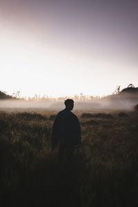 Rear view of man standing on field against sky