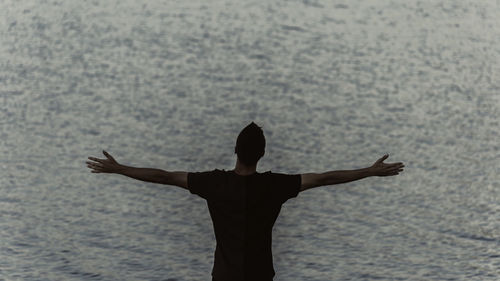 Rear view of woman with arms raised standing in sea