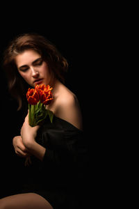 Portrait of young woman holding bouquet against black background