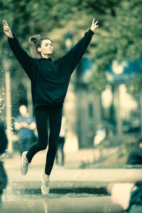 Young woman with arms raised jumping against fountain