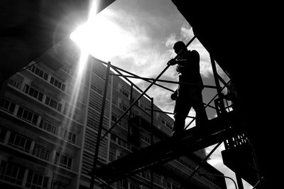 Low angle view of silhouette man working on building against sky