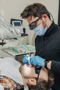 Dentist examining patient's teeth with equipment in clinic