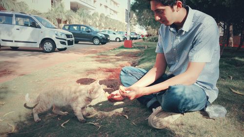 Side view of man feeding cat on grass in park