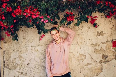 Portrait of young man standing against wall under flowering plants