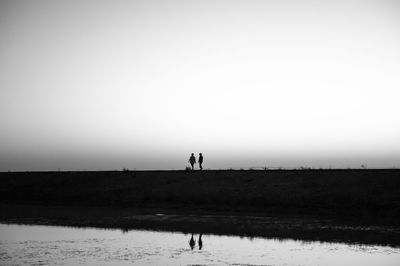 Silhouette people on beach against clear sky