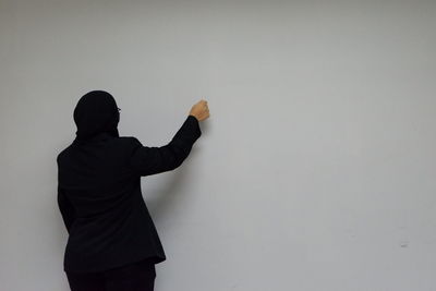 Rear view of woman in hijab gesturing while standing against gray wall