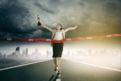 Happy businesswoman holding trophy while crossing finish line