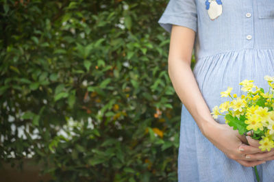 Midsection of pregnant woman holding flowers while standing at park