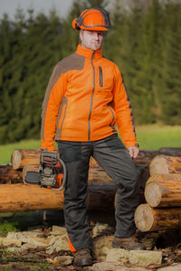 Portrait of lumberjack standing with chainsaw by logs