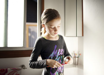 Girl putting toothpaste on toothbrush in bathroom