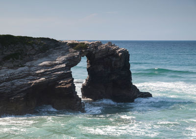 Rock formation on sea shore against sky