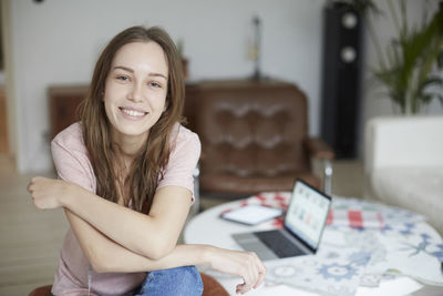 Portrait of smiling fashion designer sitting by table at home