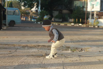 Side view of cute baby boy skateboarding on street in city