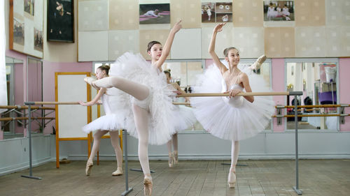 In ballet hall, girls in white ballet skirts are engaged at ballet, rehearse attitude